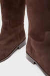 A close-up of a pair of brown suede riding boots with low heels.