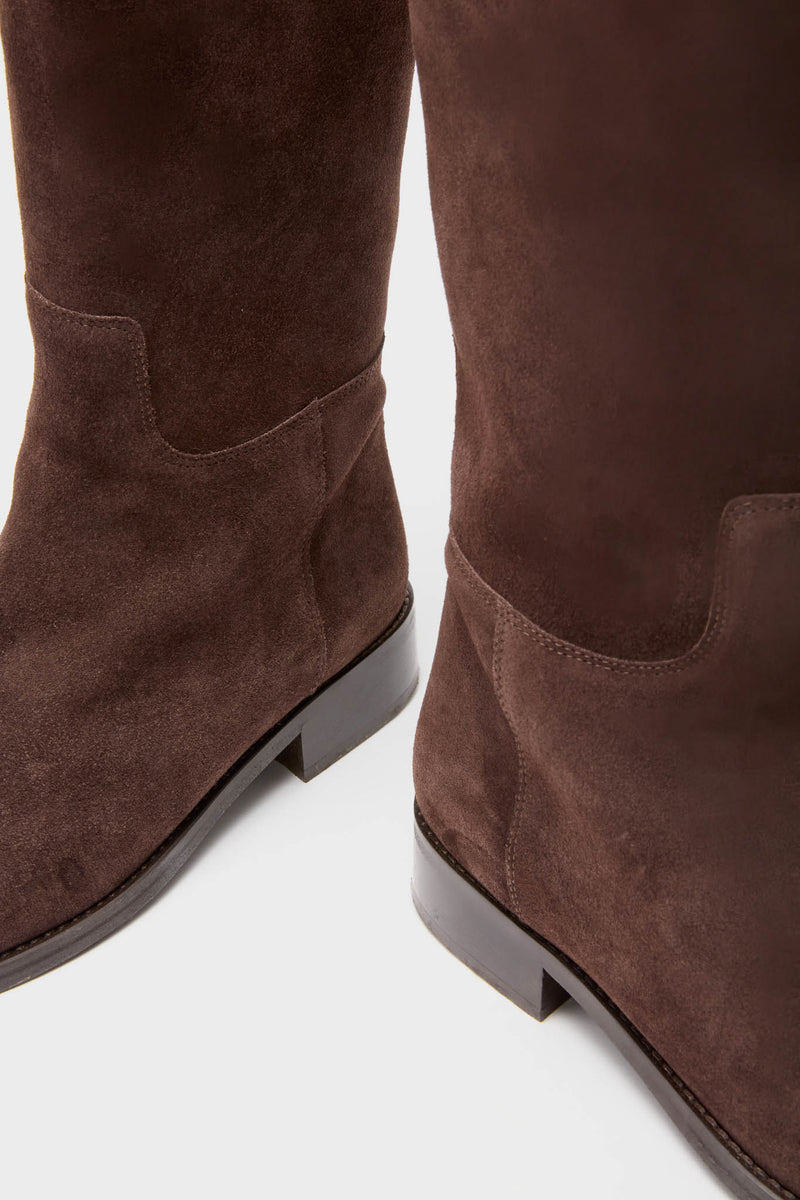 A close-up of a pair of brown suede riding boots with low heels.