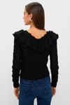 Woman in Black Pointelle Knit Sherry Top featuring a lace-trimmed ruffle collar, paired with fitted jeans, embodies classic elegance and effortless style, perfect for a high-end, fun look.