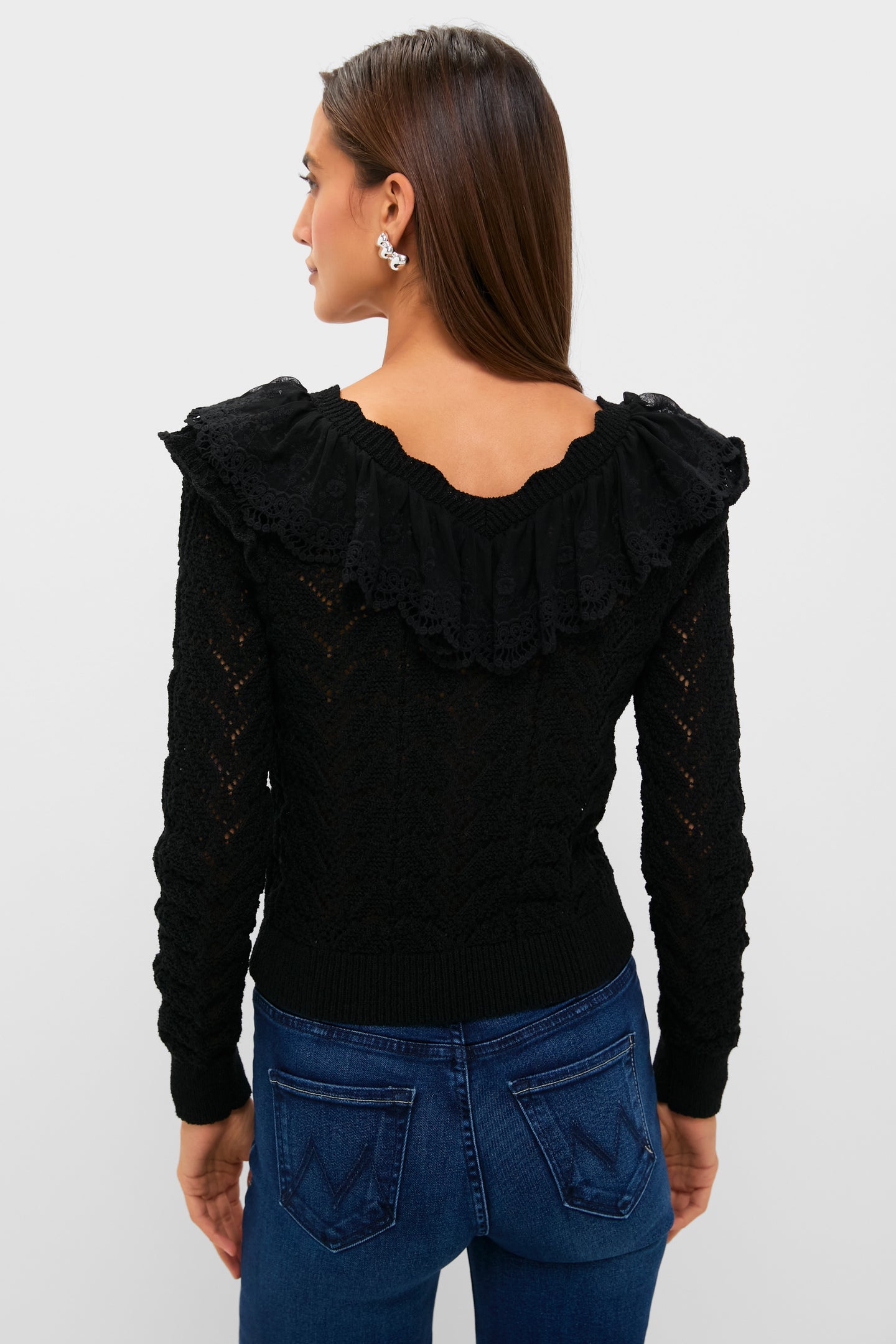 Woman in Black Pointelle Knit Sherry Top featuring a lace-trimmed ruffle collar, paired with fitted jeans, embodies classic elegance and effortless style, perfect for a high-end, fun look.