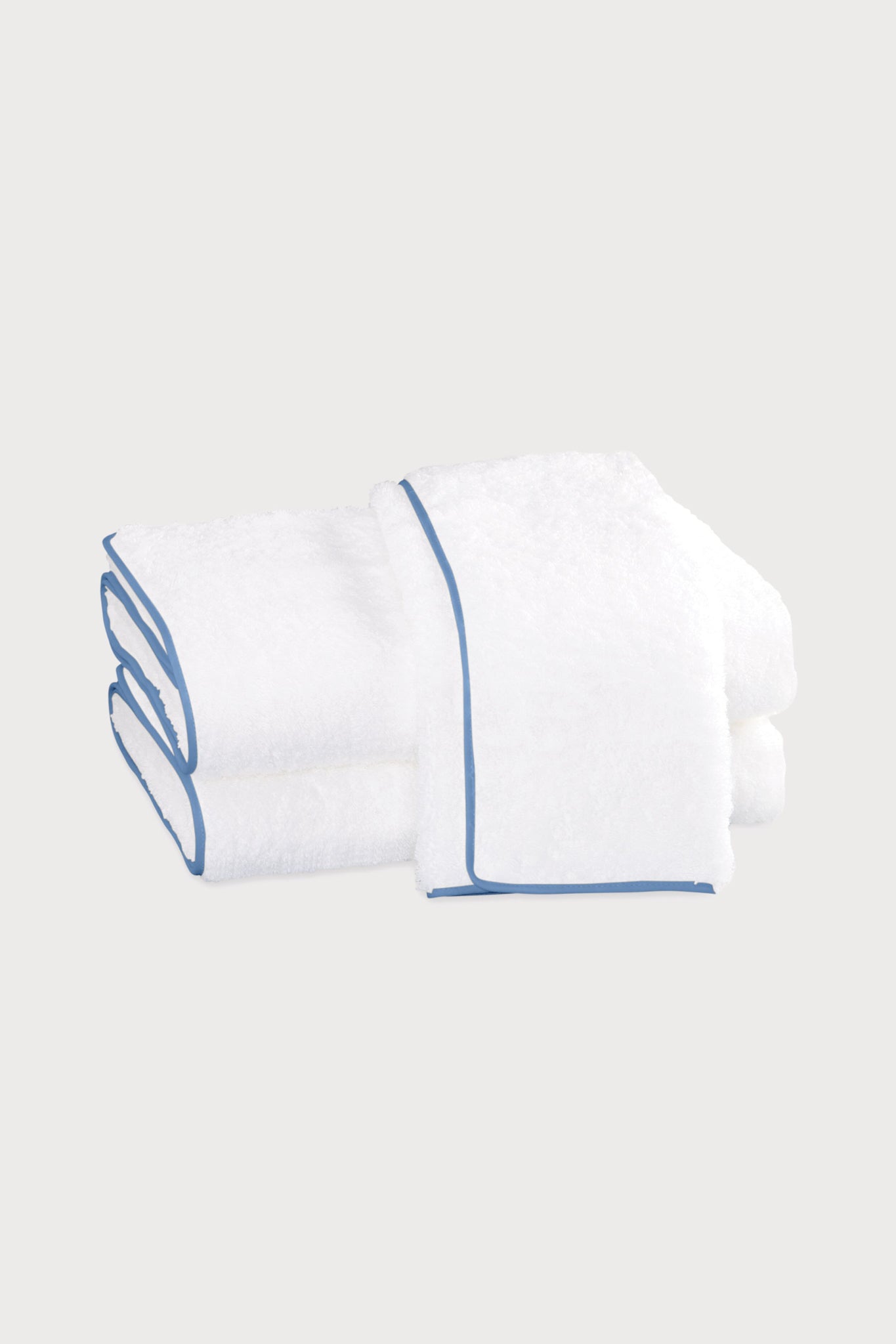 Two neatly folded white Matouk towels with blue trim, crafted from Egyptian cotton by Matouk, are stacked on a plain light background.