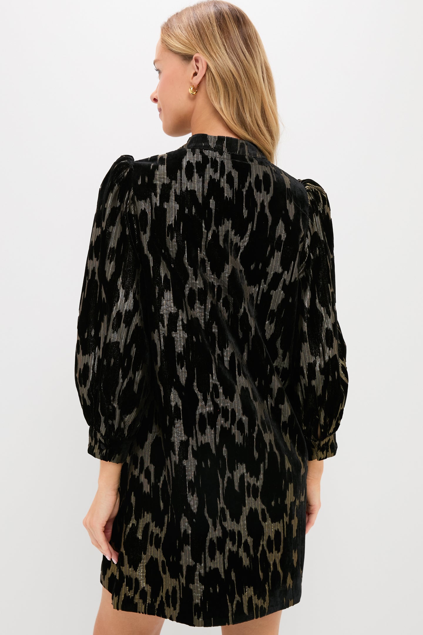 A blonde woman models a Pomander Place black, long-sleeved animal print occasion dress, shown from the back against a plain white background.