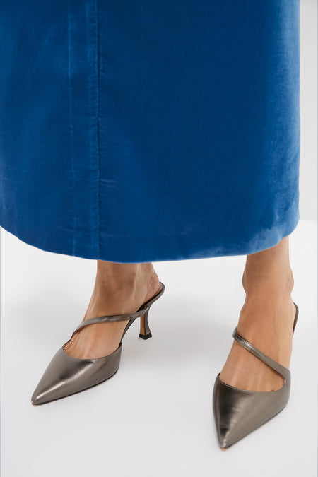 Person wearing Gunmetal Leather Mimi Heels with a pointed toe and diagonal strap, styled with a cobalt-blue skirt for a classic, effortless, and high-end look.