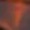The image is very blurry and indistinct, making it difficult to identify any specific objects or details. Predominantly dark with some vibrant red and orange tones.