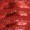 Close-up of a red, shiny, textured surface with overlapping, scale-like patterns that shimmer in the light.