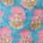 Blurry image of a patterned fabric with pink and green floral shapes on a light blue background.