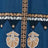 A close-up of blue fabric with geometric patterns and white embroidered designs, featuring a vertical decorative strip and triangular tribal-inspired accents.