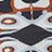 A close-up of a geometric patterned textile featuring black, white, brown, and orange shapes arranged in a symmetrical design.