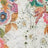 Close-up of fabric with a colorful floral print featuring various flowers, green leaves, and brown foliage on soft white cotton.