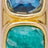 Close-up of two square gemstones, one sapphire-blue and one emerald-green, set in gold-colored metal.