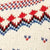 Close-up of a knitted fabric featuring a red, blue, and white geometric pattern on soft cream yarn.