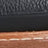 Close-up of a shoe showing black textured leather, a black midsole, and brown outsole with visible white stitching.
