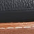 Close-up of a shoe showing black textured leather, a black midsole, and brown outsole with visible white stitching.