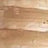 A close-up view of a light-colored wooden surface with visible grain patterns and natural texture.