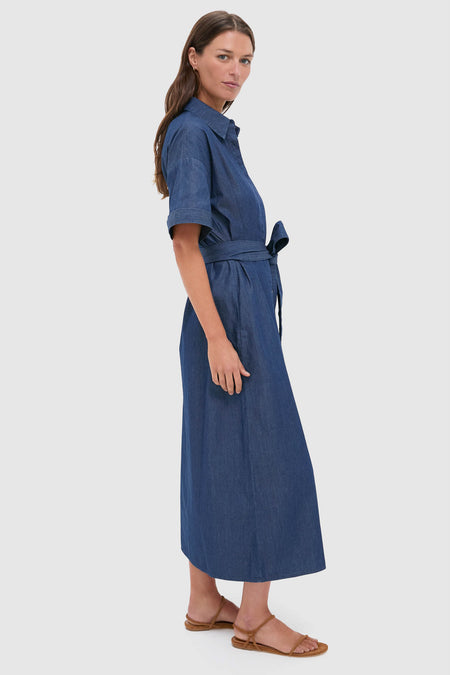 Model wearing the Dark Denim Zacara Dress, a classic, effortless denim shirt dress with a self-tie waist, short sleeves, and sandals; embodies fun, high-end style.