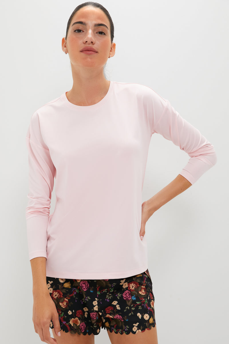 A woman wears a Tnuck Sport light pink crewneck long sleeve shirt with SPF protection and black floral shorts.