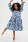 Young girl in a classic, long sleeve floral button-front dress, striking a playful pose. Effortless style with frilled collar and ric rac details, paired with fun, glittery shoes.