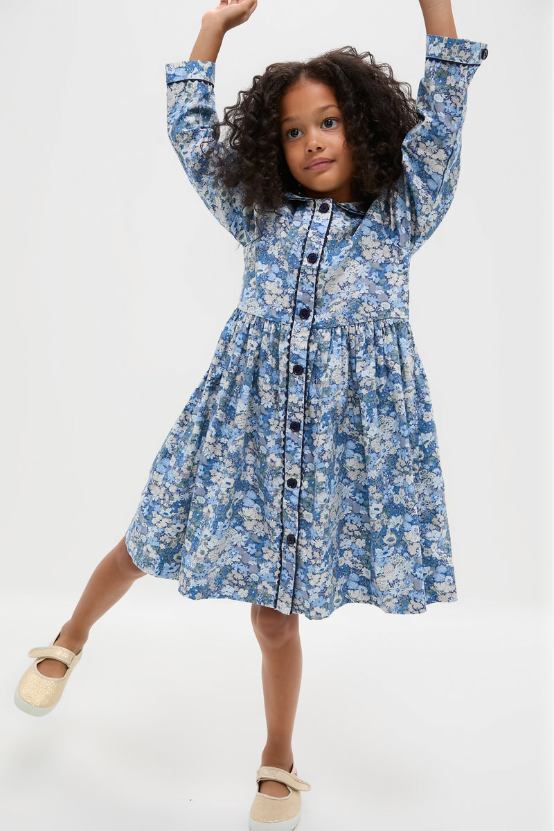 Young girl in a classic, long sleeve floral button-front dress, striking a playful pose. Effortless style with frilled collar and ric rac details, paired with fun, glittery shoes.