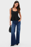 Woman models the Black Sleeveless Decker Peplum Top with a classic peplum silhouette, paired effortlessly with dark-blue flared jeans, exuding a fun, high-end style.