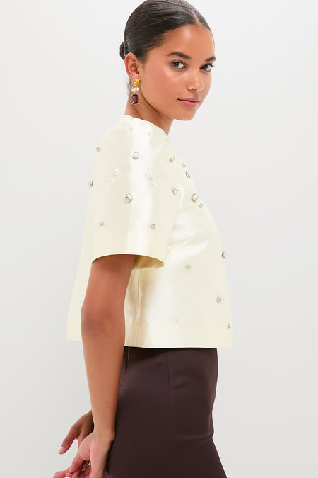 Model in profile wearing the classic Ivory Olivia Top, an effortless high-end cropped satin design with fun pearl and rhinestone embellishments, paired with a fitted dark-brown skirt.