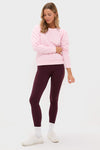 A woman poses against a plain background in a Tnuck Sport light pink quilted sweatshirt with puff sleeves, paired with dark purple leggings, white socks, and white sneakers.