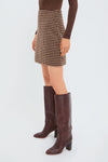 Model wearing the classic Noir and Noisette Mimi Mini Skirt with an effortless check pattern, styled with high-end, fun dark-brown knee-high boots.
