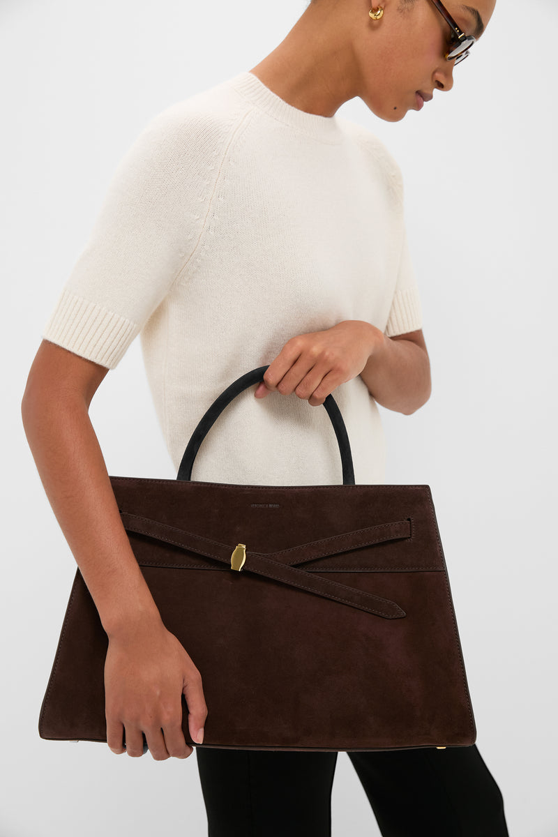 Woman holding the Espresso Large Suede Veronica Beard Dash Bag, a classic and high-end dark-brown tote with an effortless trapezoidal design and fun, versatile straps.