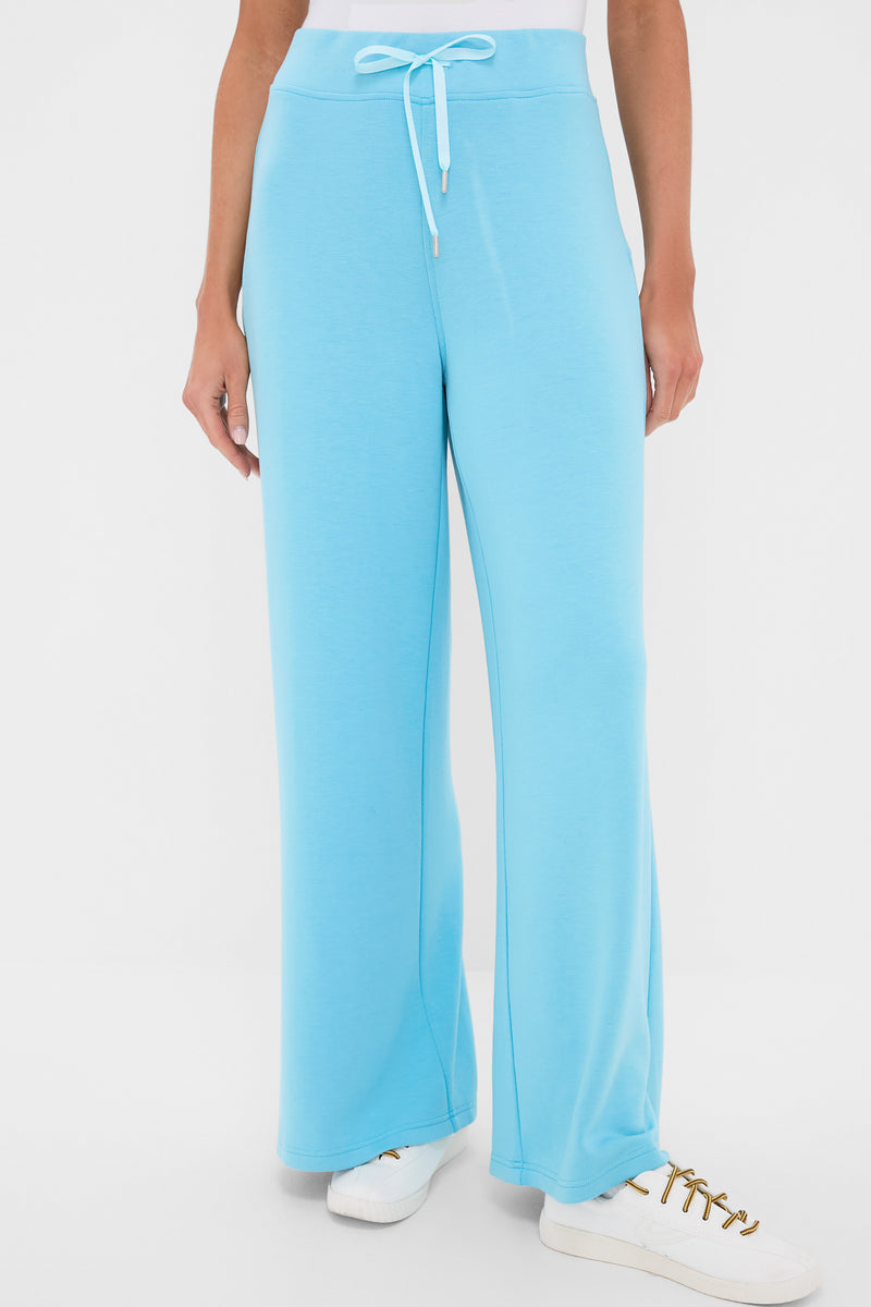 A person wears Tnuck Sport light blue wide-leg lounge pants with a drawstring waistband and white sneakers, highlighting the ultra-soft comfort of these sweatpants.