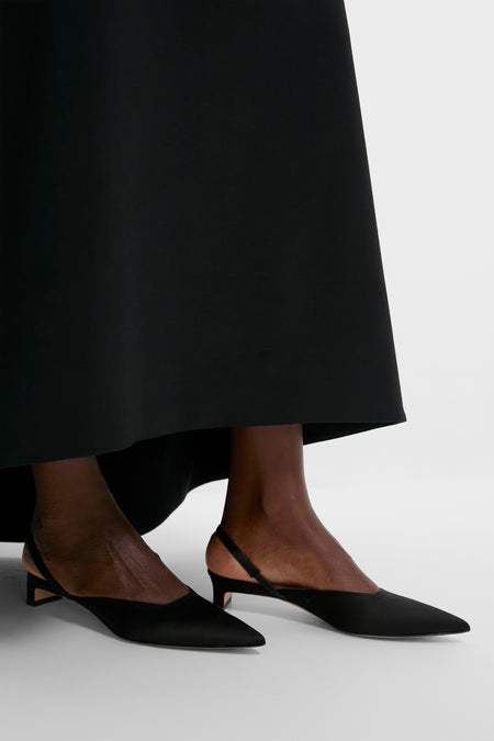 A person wears an Emilia Wickstead Black Birdseye Suiting Skirt and black pointed-toe slingback flats, standing on a white surface.