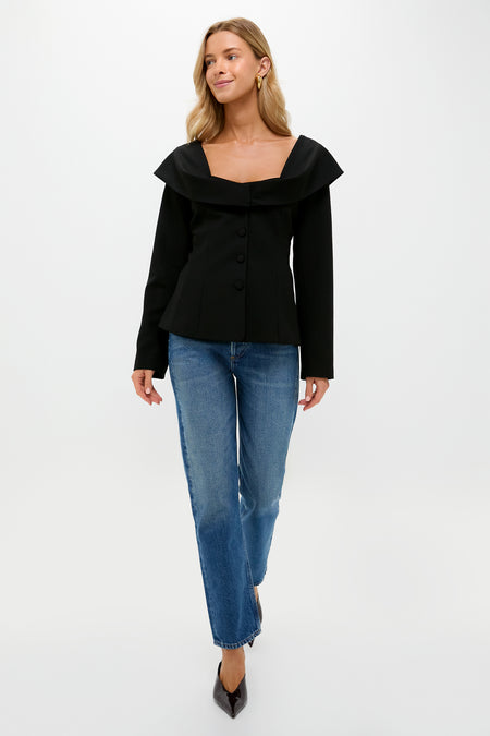 A woman walks forward against a plain white background wearing a black Tuckernuck Monroe Top with a scoop neck and blue straight-leg jeans.