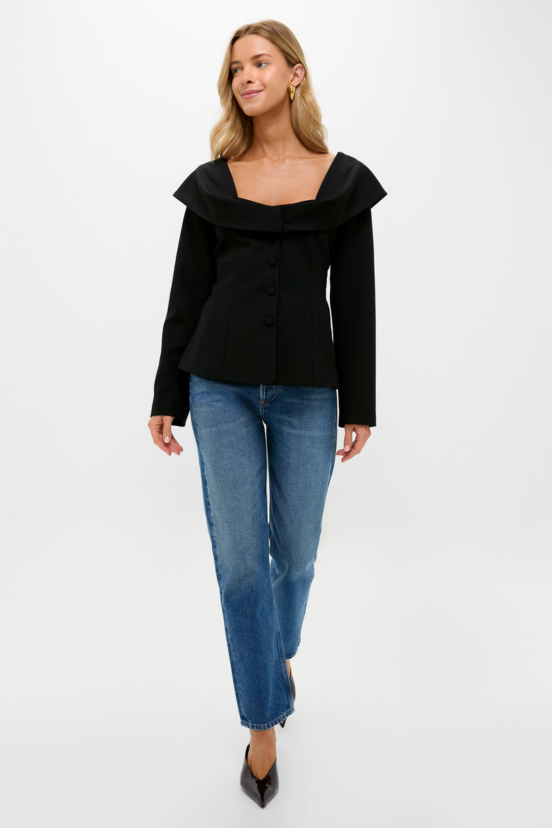 A woman walks forward against a plain white background wearing a black Tuckernuck Monroe Top with a scoop neck and blue straight-leg jeans.