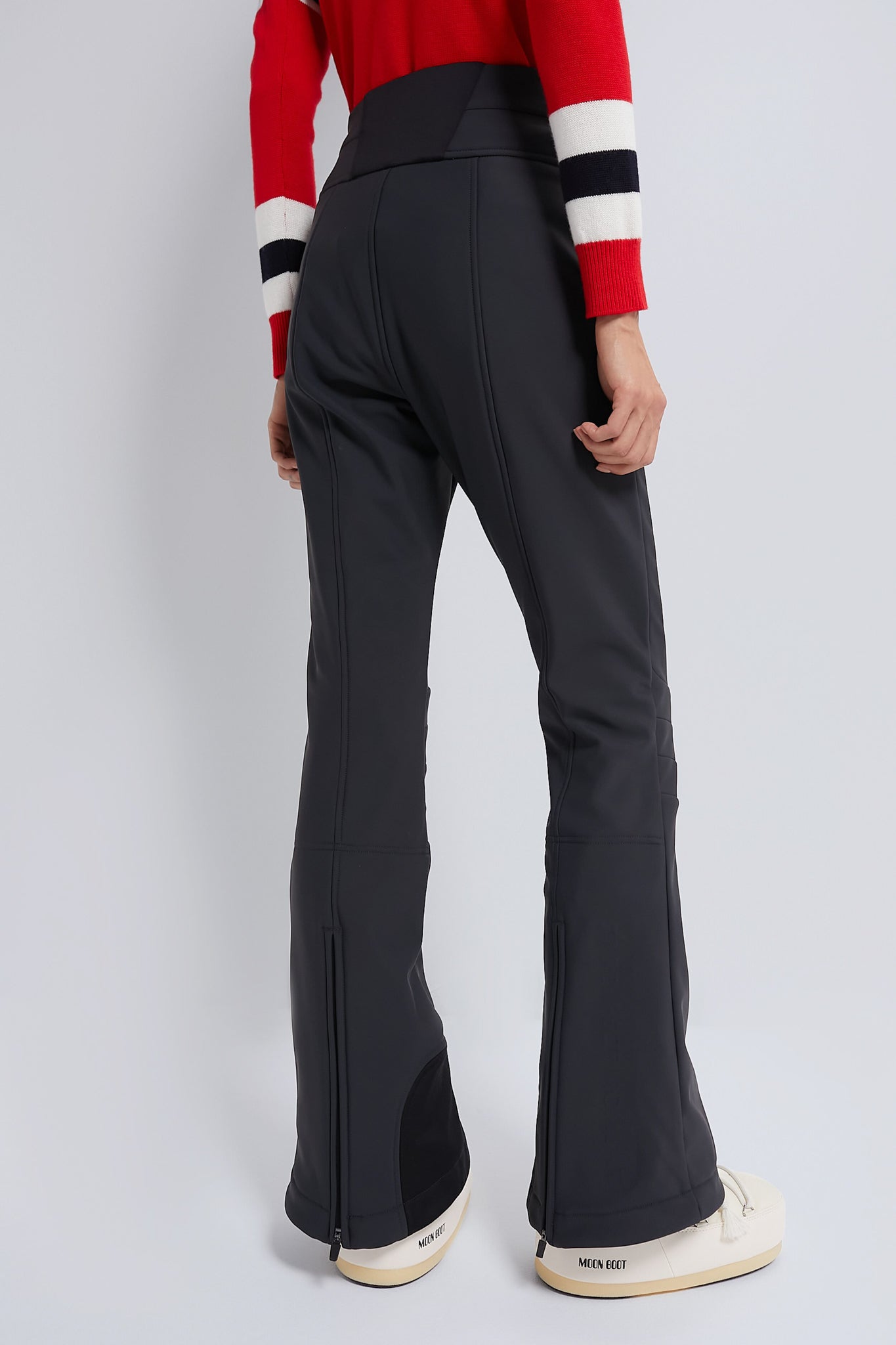 Black Aurora High Waist Ski Pant with sleek, flared design and zippers at hems, paired effortlessly with white Moon Boot winter boots for a classic, high-end look.