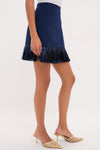 Navy Metallic Fringe Francie Mini Skirt with a classic metallic fringe trim, paired effortlessly with high-end gold strappy mules, exudes a fun and sophisticated style.