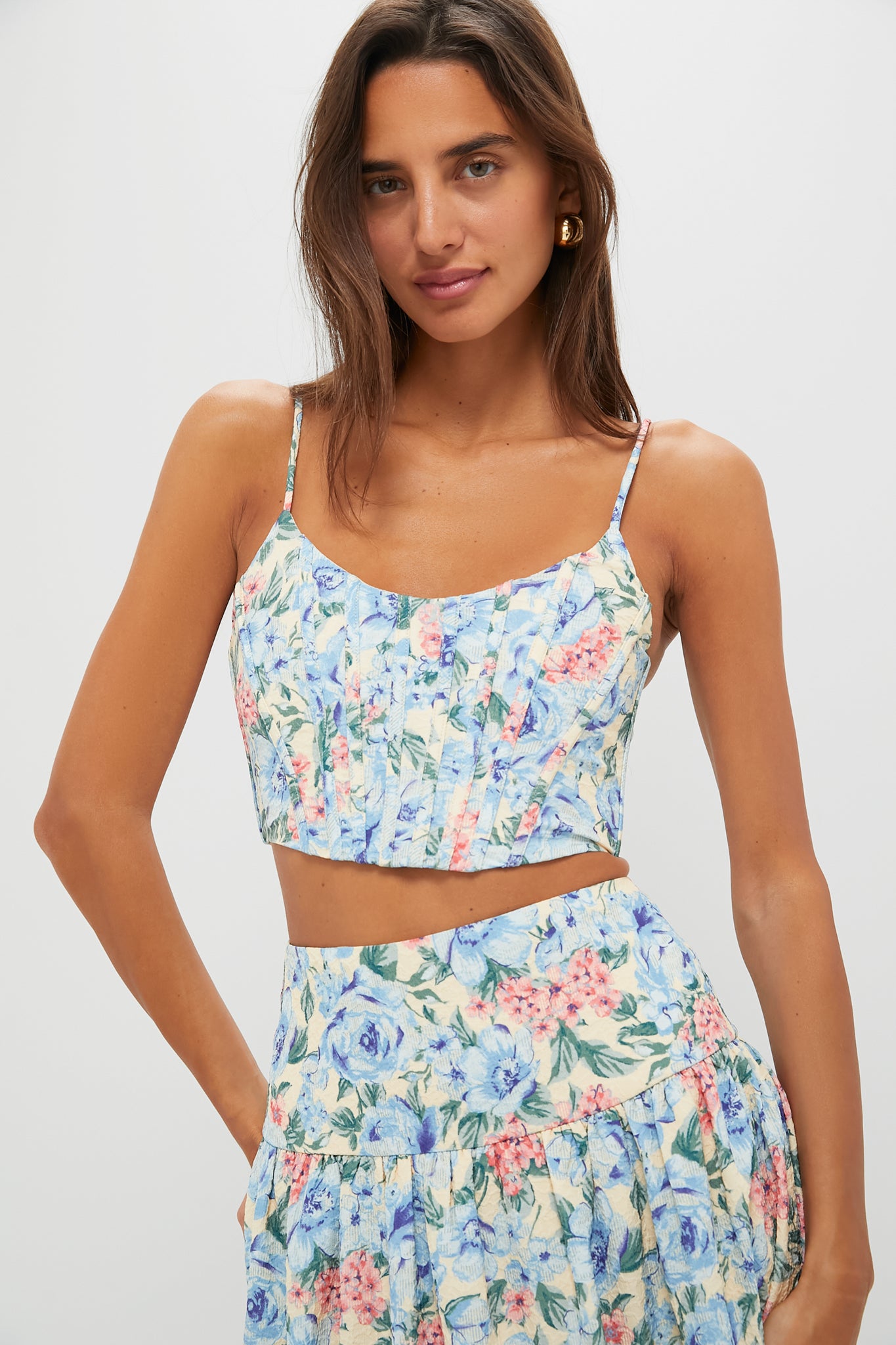 A woman in a Moon River blue floral tank top with a smocked back and matching high-waisted skirt stands in a simple, well-lit setting.