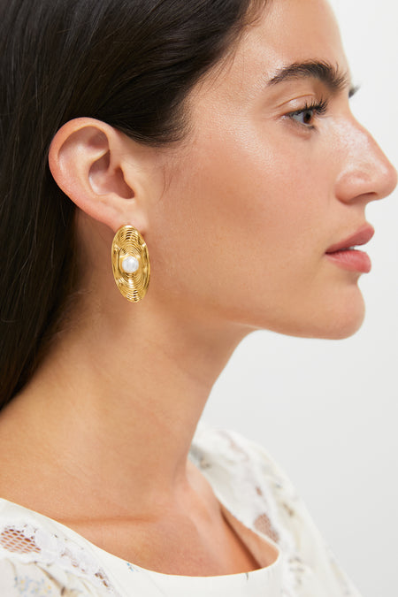 Side profile of a woman wearing Gold Trumbull Earrings: classic gold oval studs with a central pearl, exuding effortless elegance and high-end style.
