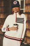 Person wearing the White Flag Heiden Quarter Zip, featuring classic red piping and retro stripes, holds a coffee cup, embodying an effortlessly cool and fun high-end style.