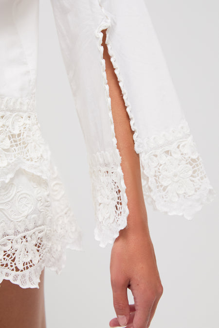 A close-up of a persons arm wearing a Sea New York white blouse featuring lace details, a sleeve slit, and delicate soutache embroidery.