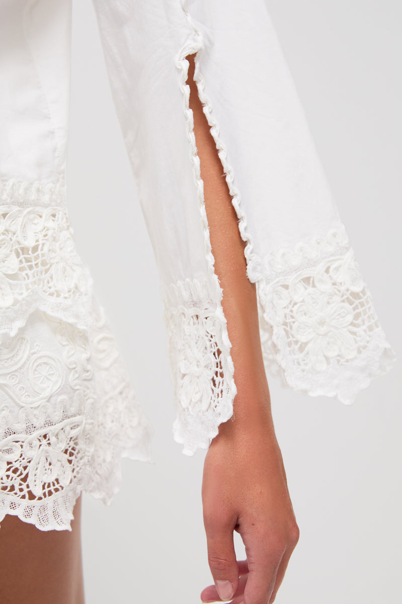 A close-up of a persons arm wearing a Sea New York white blouse featuring lace details, a sleeve slit, and delicate soutache embroidery.