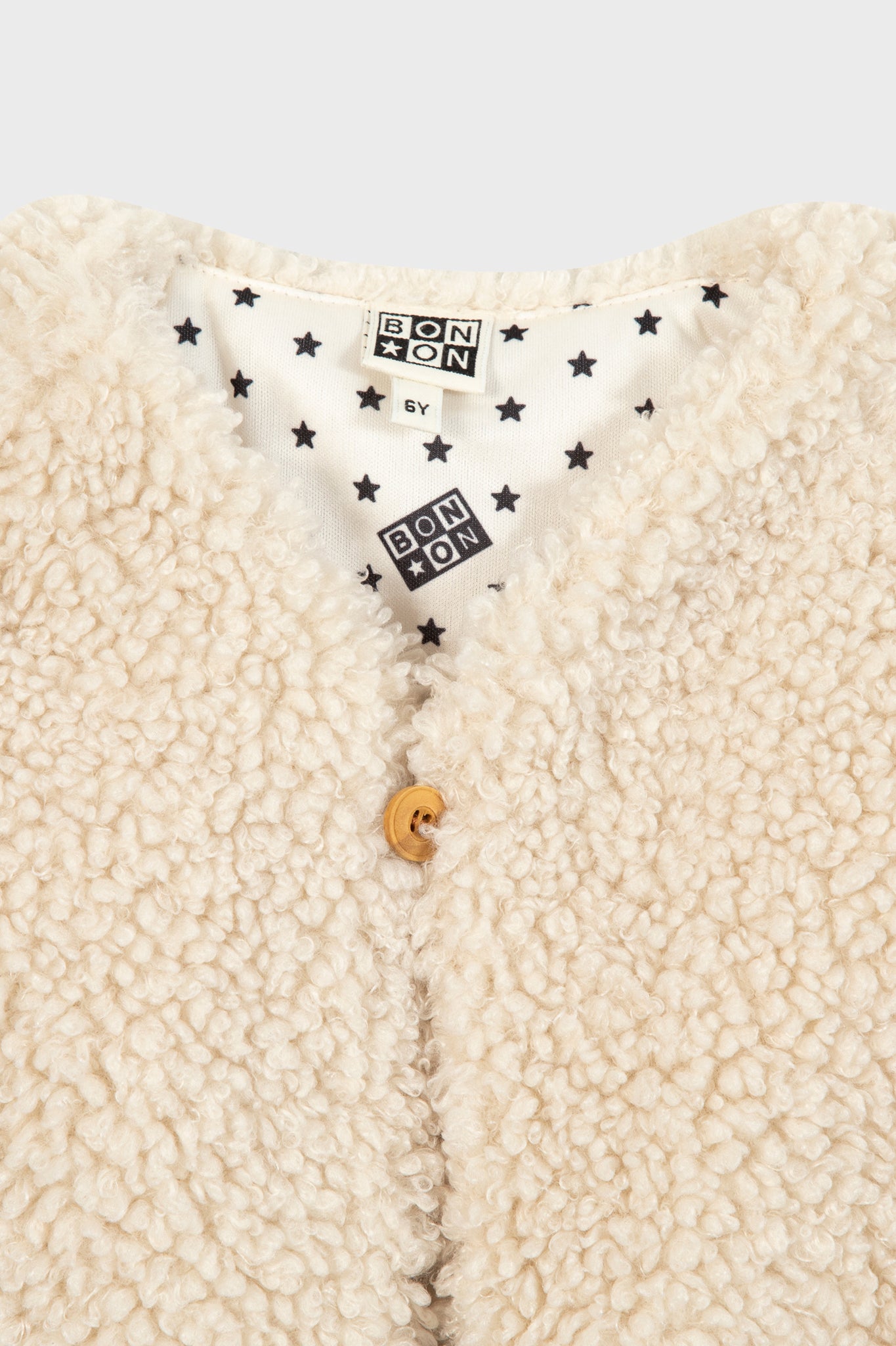 Cream Teddy Vest with curly fleece, a classic single-button closure, and fun star-patterned lining, embodies effortless, high-end style for your child's wardrobe.