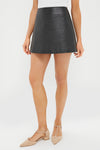 A person wears a Tuckernuck black faux leather A-line mini skirt, a white sleeveless top, and beige pointed-toe flats.