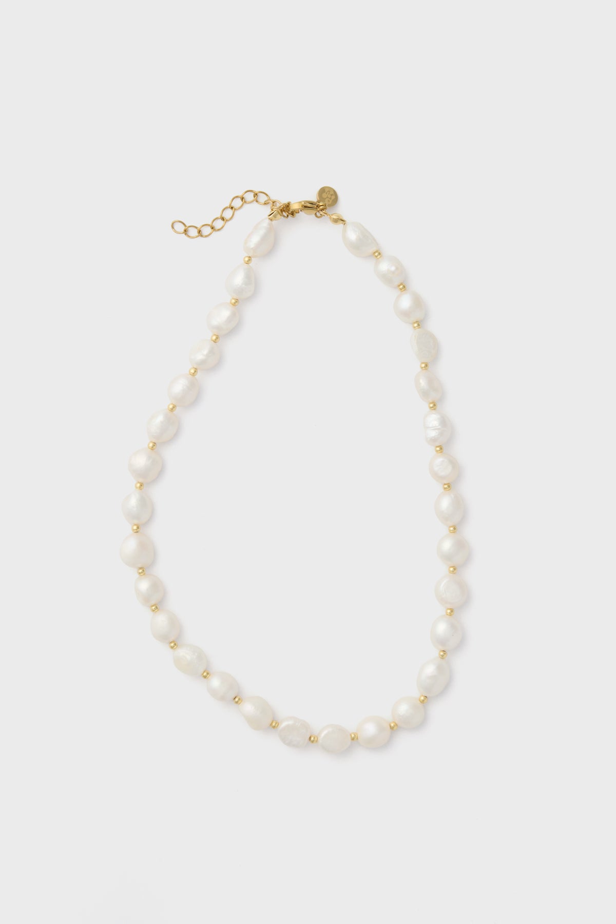 The Petit Moments freshwater pearl necklace features irregular white pearls, small gold beads, a gold clasp, and an adjustable chain for a perfect fit.