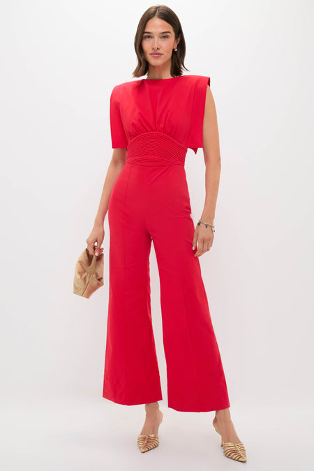 Woman in a sleek, vibrant red jumpsuit, accessorized with an elegant beige clutch and gold-tone mules, embodying a classic, effortless, and high-end style.
