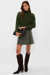 Model in a classic, effortless look wearing the Olive Faux Leather Phillips Skirt with pleats, styled with a chunky sweater and cowboy boots, exuding fun and high-end appeal.