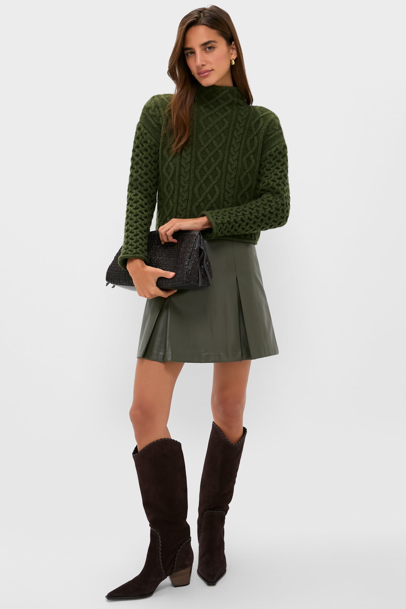 Model in a classic, effortless look wearing the Olive Faux Leather Phillips Skirt with pleats, styled with a chunky sweater and cowboy boots, exuding fun and high-end appeal.