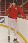 Young woman in ice rink wearing Red Shaun Quarter Zip with USA crest, effortlessly styled with retro stripe details, embodying a classic, fun, high-end winter look.