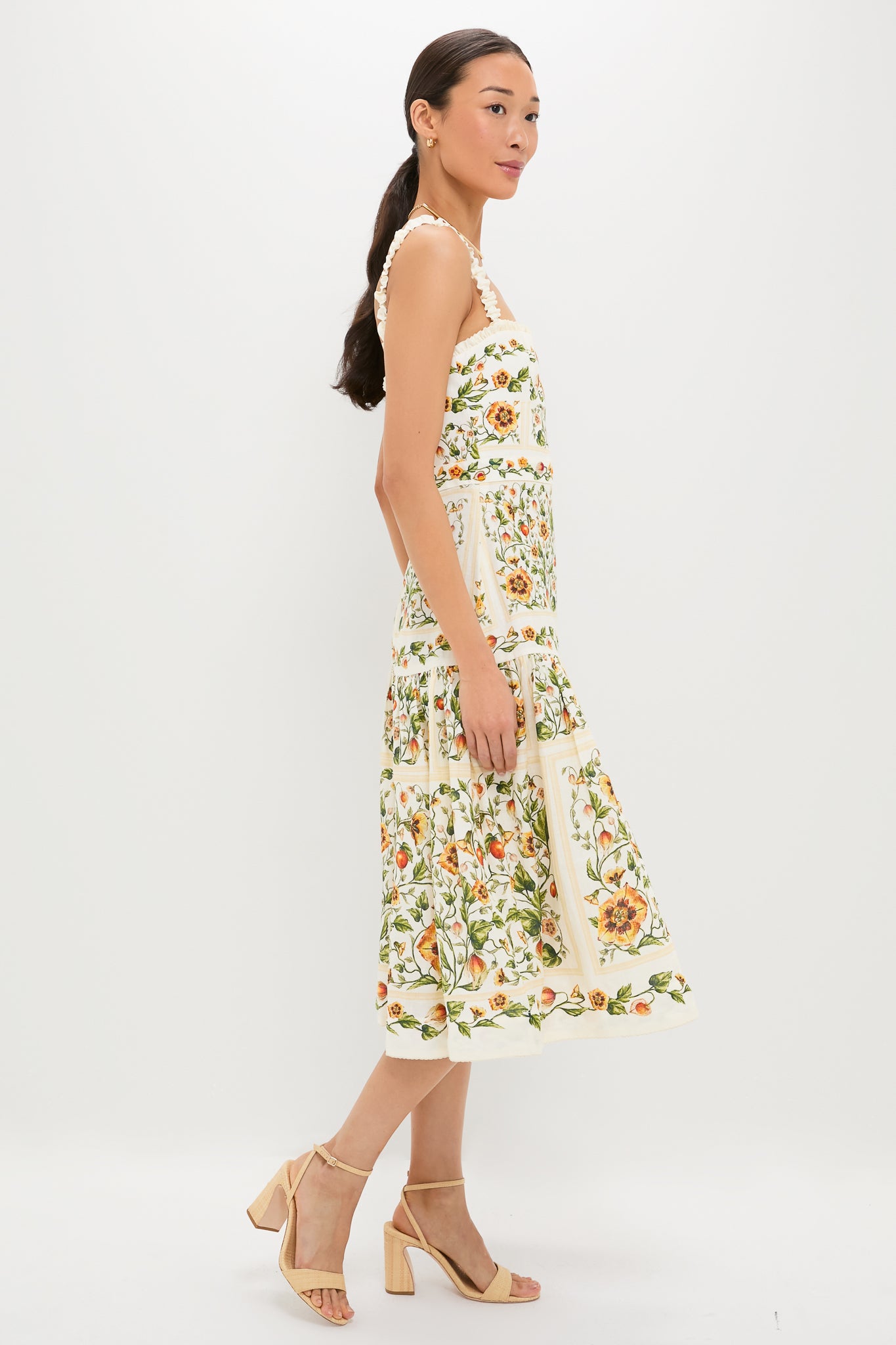 Model wearing the Uchuva Nispero Midi Dress, a classic sundress with a botanical print, ruffled straps, and flared skirt, paired with beige block-heel sandals for an effortless, high-end look.