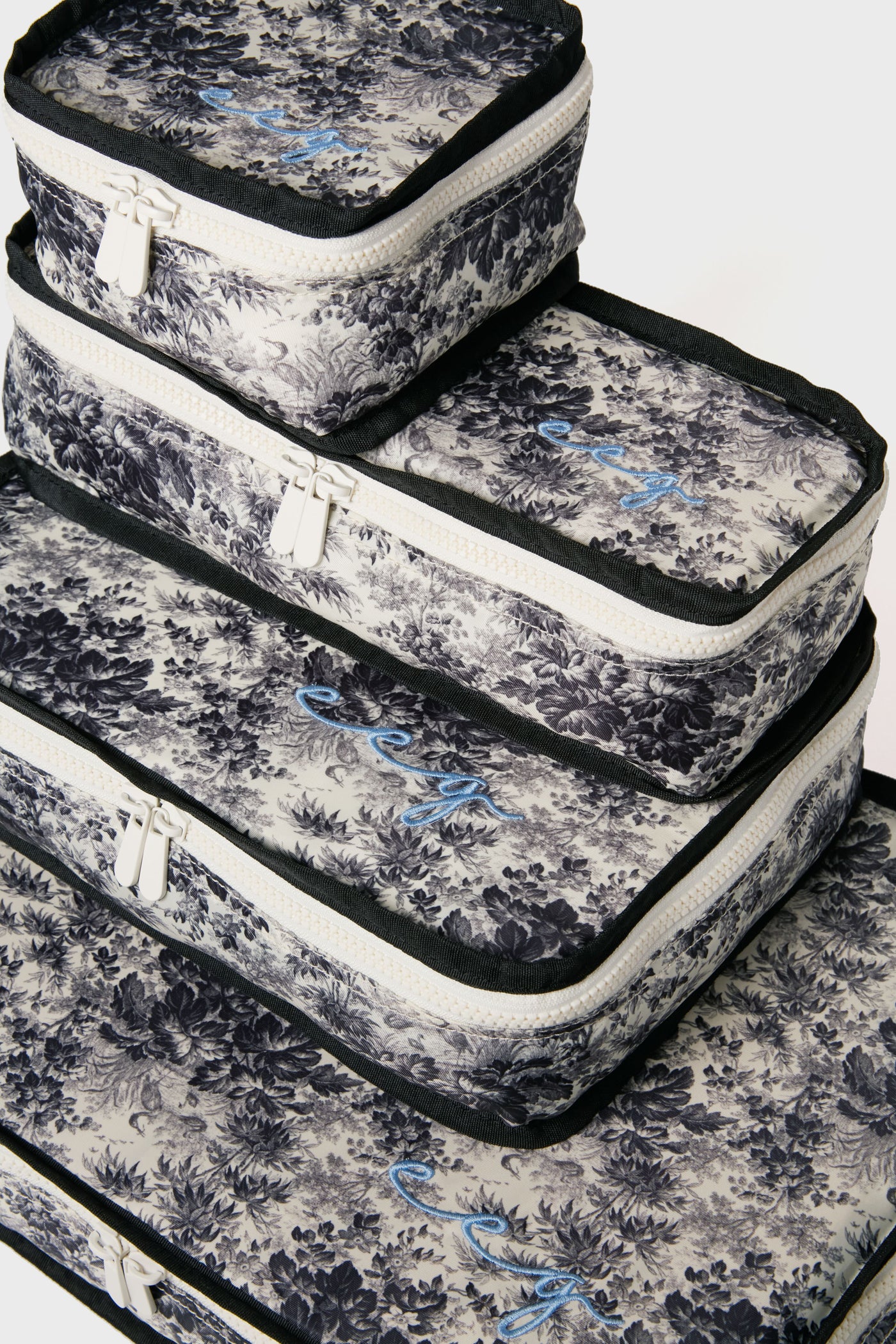 Set of four Tuckernuck Accessories packing cubes featuring black and white floral patterns, white zippers, and blue cursive embroidery—ideal for organizing travel essentials in your suitcase.
