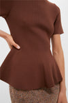 Woman wearing Chocolate Brown Knit Phoebe Peplum Top with a fitted bodice and peplum hem, paired with herringbone bottom. Classic, effortless, and fun high-end style.