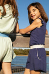 Two little girls. One wearing a navy tank and shorts with white piping. The other girl is wearing a mint tank and shorts with blue piping. 