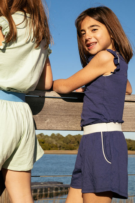 Two little girls. One wearing a navy tank and shorts with white piping. The other girl is wearing a mint tank and shorts with blue piping. 